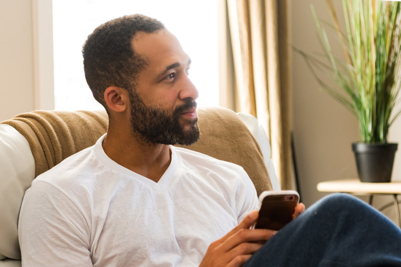 handsome Black man using his smart phone at home while relaxing - in-home detox